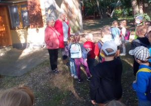 dzieci i nauczycielki stoją przed budyniem, są witane przez gospodynie terenu w KAtarzynowie