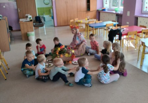 nauczycielka przebrana w jesienny stój prowadzi zajęcie, wokół niej na dywanie siedzą dzieci