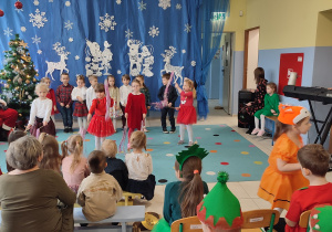 dzieci tańczą z szarfami, za nimi świateczna dekoracja
