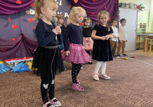 trzy dziewczynki występują przed zaproszonymi gośćmi, w tle dekoracja