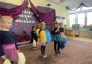 grupa dzieci z pomponami wystepuje przed zaproszonymi gośćmi, w tle dekoracja
