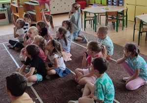 dzieci siedzą na dywanie , słuchają nauczycielki