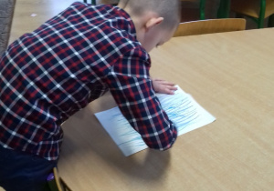 chłopiec stojąc przy stoliku kreśli linie pastelą na kartce