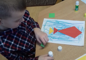 chłopiec siedzi przy stoliku i zgina kolorowe papierowe origami -kwadraty
