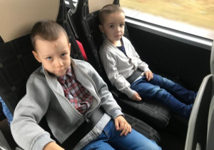 dwoje dzieci siedzi na fotelach w autokarze