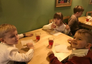 dzieci siedzą przy stolikach i jedzą ciasteczka