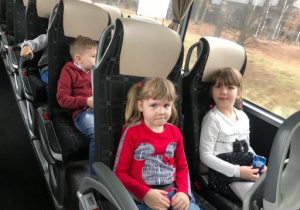 troje dzieci siedzi na fotelach w autokarze