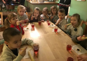 grupa dzieci siedzi przy stolikach i je ciasteczka