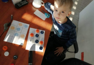 chłopiec siedzi nprzy stole i koduje za pomocą kolorowych nakrętek