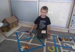 chłopiec siedzi na dywanie i wykonuje zadanie matematyczne z samochodzikami