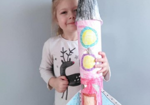 dziewczynka trzyma w dłoniach wielką rakietę z kartonu