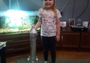 dziewczynka pokazuje rakietę z kartonu i folii aluminiowej
