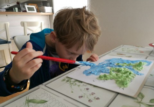 chłopiec maluje roznącymi farbami obrazek kuli ziemskiej