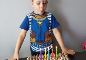 chłopiec przy torcie urodzinowym, dmucha w świeczki
