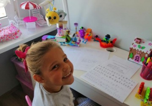 dziewczynka siedzi przy stole, na którym leżą karty pracy
