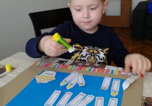 chłopiec nakleja pokolorowane świeczki na karton