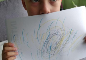 chłopiec pokazuje pracę wykonaną podczas zabawy muzycznej "Rysujemy pogodę"
