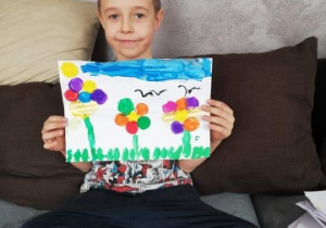 chłopiec pokazuje wykonaną przez siebie pracę z kwiatami