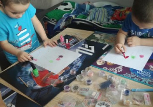 dwaj chłopcy lakierami do paznokci malują obrazki dłoni