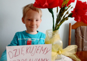 chłopiec siedzi przy stole, wazon z kwiatami i napis dla medyków
