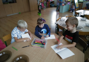troje dzieci z grupy Słoneczka siedzi przy stoliku i rysuje kredkami