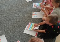 dzieci siedzą na dywanie i wypychają kolorowe kropki z kartoników