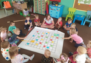 grupa dzieci siedzi na podłodze i układa kolorowe kropki na macie do kodowania