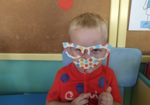 chłopiec trzyma przy twarzy okulary w kropki