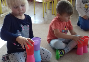 dziewczynka i chłopiec układają wieże z kubków