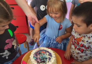 dziewczynka kroi urodzinowy tort, obok stoją dzieci