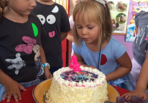 dziewczynka dmucha świeczkę na torcie, obok stoją dzieci