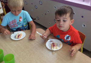 dwóch chłopców siedzi przy stoliku i je tort