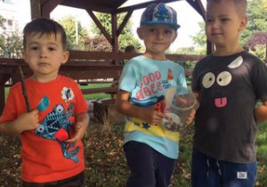 trzech chłopców stoi przy altanie w przedszkolnym ogrodzie, jeden z nich trzyma pudełko ze ślimakami
