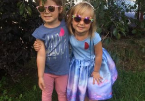 dwie dziewczynki stoją na trawie, mają założone okulary p/słoneczne