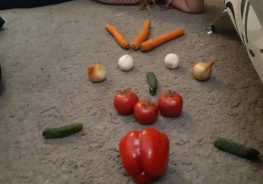 dziewczynka leży na dywanie obok wykonanej kompozycji z warzyw