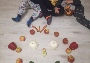 trzej chłopcy siedzą na podłodze i prezentują swoją kompozycję z warzyw