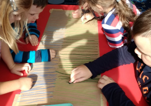 dzieci przy stoliku kreślą linie pastelami