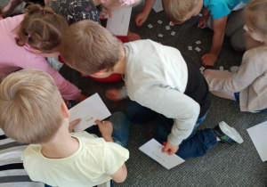 grupa dzieci na dywanie zbiera kartoniki z literami