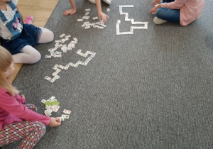 dzieci siedzą na dywanie i układają tafle domina
