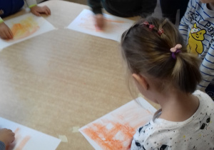 dzieci stoją przy stole i kreślą ślady pastelą