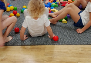 dzieci siedzą na podłodze i bosymi stopami zbierają piankowe klocki i kolorowe piłeczki