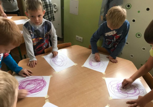 dzieci przy stoliku kreślą koła fioletowymi pastelami