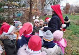 grupa dzieci i ich nauczycielka na dworze szukają wskazówek od Mikołaja