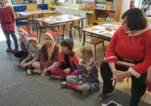 grupa dzieci siedzie na dywanie, obok na krzesełku siedzi nauczycielka, wszyscy ubrani na czerwono