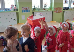 dzieci stoją w rzędzie , podają sobie prezent opakowany w czerwony papier