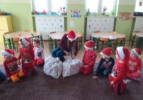dzieci siedzą na dywanie, na krzesełku siedzi nauczycielka, która rozdaje prezenty
