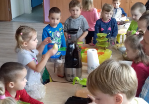dzieci przy stole przygotowują owoce na soki