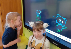 dwie dziewczynki przy tablicy interaktywnej rysują misie