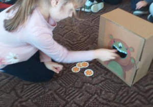 dziewczynka wrzuca do pudełka z misiem żetony matematyczne
