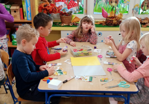 dzieci siedzą przy stoliku, wycinają obrazki z warzywami i owocami